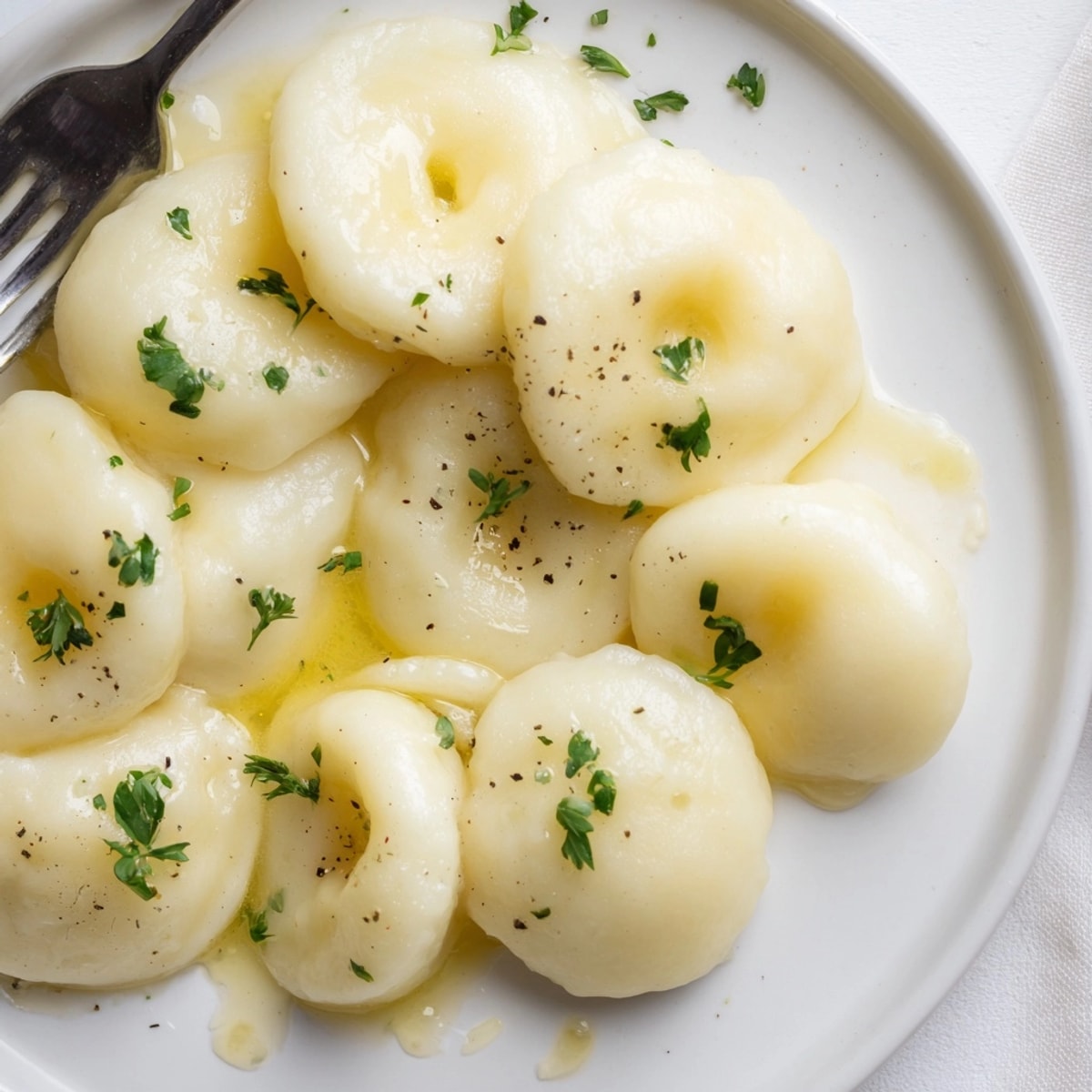 Close-up image of homemade Silesian Dumplings recipe; dimpled and topped with parsley flecked butter.
