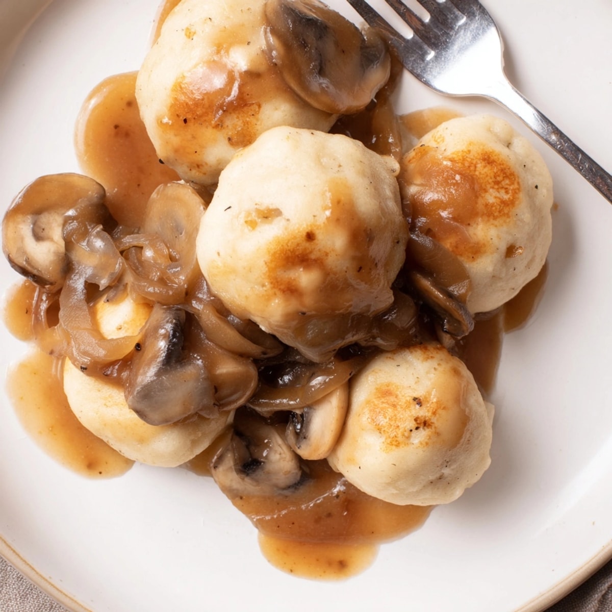 Pieczone kluski ziemniaczane polane bogatym wegańskim sosem grzybowym idealny przepis na komfortowy posiłek.