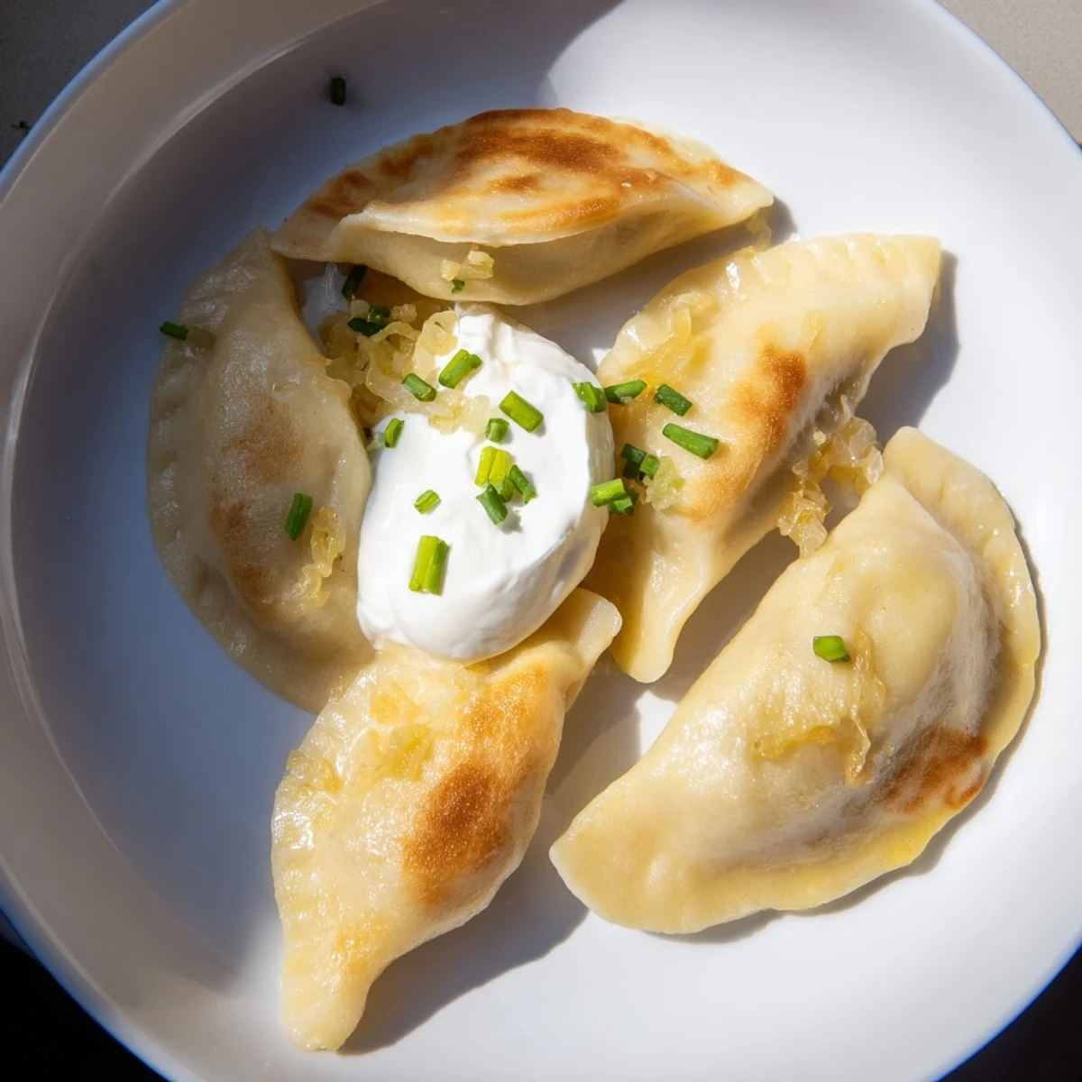 Pierogi z nadzieniem ziemniaczano-serowym: usmażone na złoto pierogi podane z kwaśną śmietaną i szczypiorkiem.