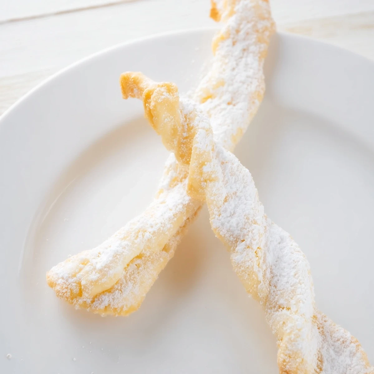 Pyszne, chrupiące ciasteczka anielskie, świeżo usmażone i gotowe do obfitego oprószenia cukrem.