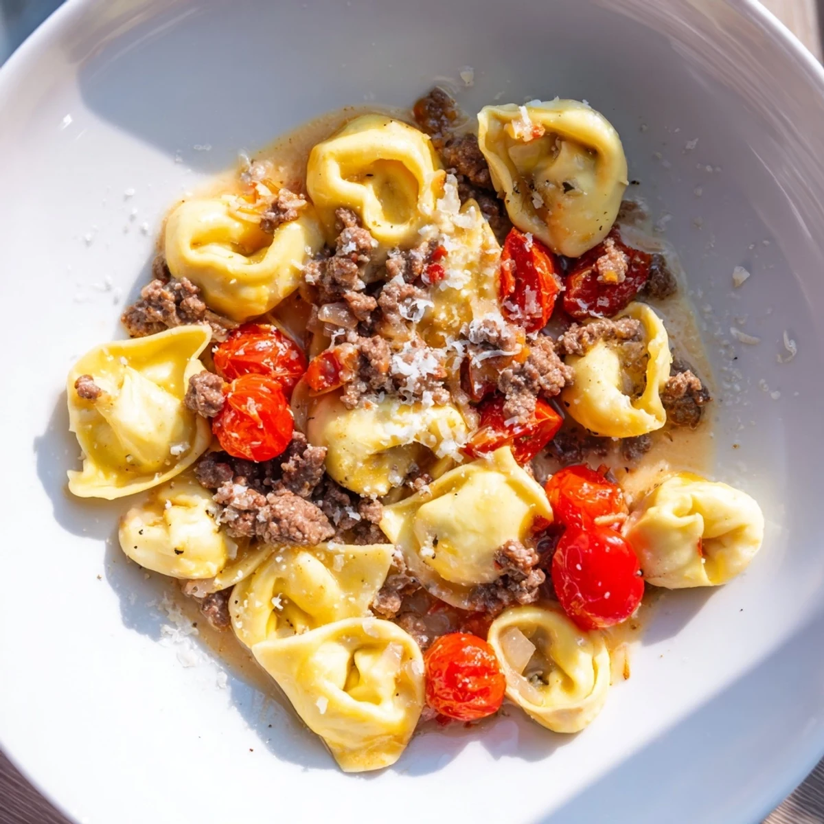 Close-up of a flavorful Tortellini Beef Soup, with visible ground beef and cherry tomatoes.