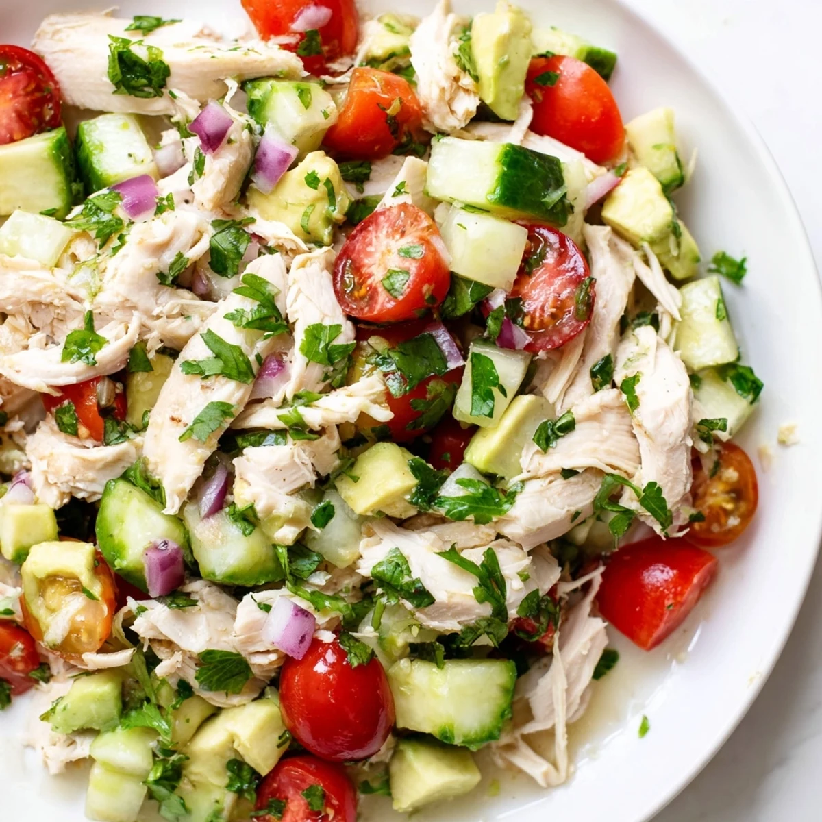Creamy avocado chicken salad with visible chunks of avocado and bright red tomatoes.