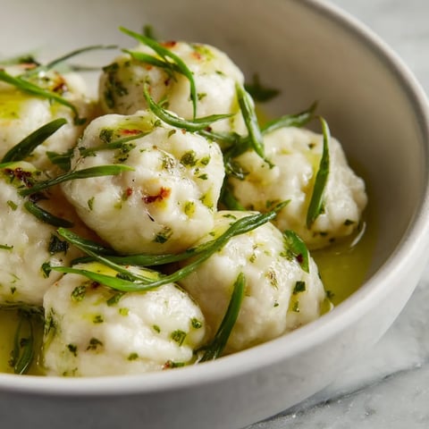 W white bowl with green herbs on top of it, there are Tatra Cheese Dumplings with Chive Oil.