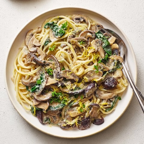 Pojemne miski z makaronem w kremowym sosie grzybowym, podane z świeżymi ziołami.  