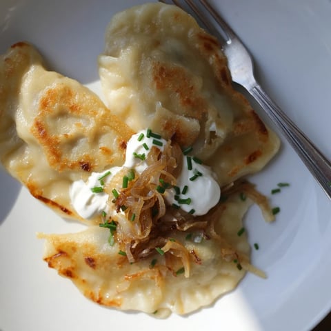 Delikatne pierogi ziemniaczane i serowe, podane z kwaśną śmietaną i cebulką.