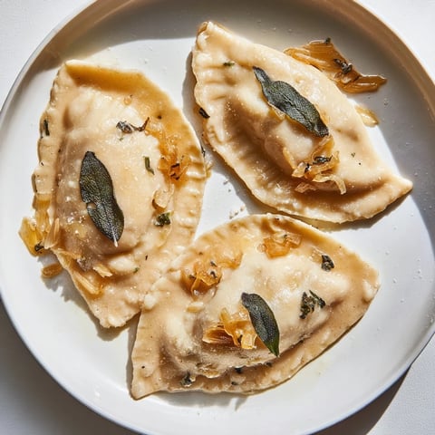 Golden-brown pierogi with sweet potato filling, served with fried onions and fresh sage leaves.