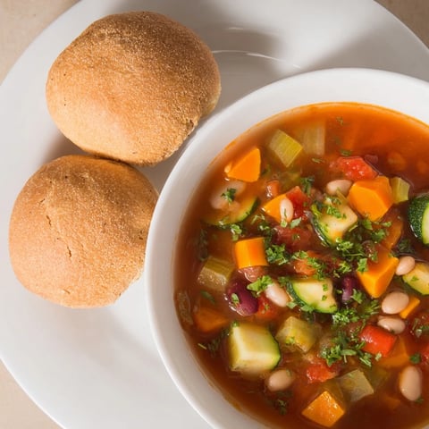 Fluffy homemade bread rolls, golden-brown and warm, perfect with a bowl of hearty bean-and-vegetable soup.