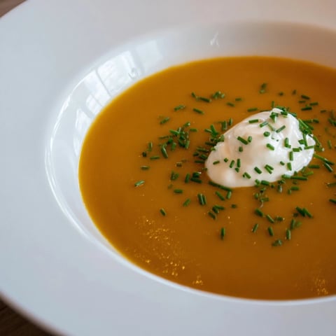 Creamy pumpkin soup with sour cream and fresh bread, ready for a comforting meal.