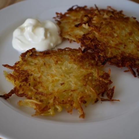 Złociste, chrupiące polskie placki ziemniaczane, podane na talerzu z kremową śmietaną i jabłkami.