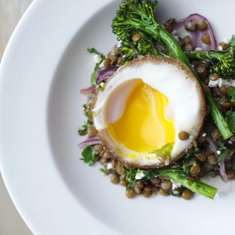 French Lentil Salad With Broccolini and Soft-Cooked Eggs arranged in a ceramic bowl, featuring vibrant green broccolini and jammy halved eggs.