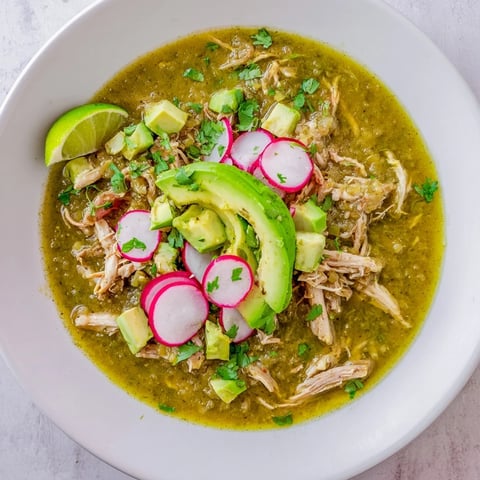 A vibrant bowl of Chicken Chili Verde with tender shredded chicken in a bright green tomatillo sauce, topped with fresh cilantro and avocado.
