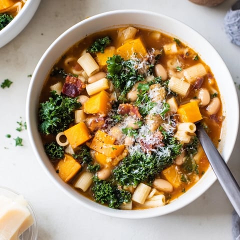 Fall Minestrone soup in a rustic bowl, featuring butternut squash, kale, creamy white beans, and ditalini pasta topped with crispy pancetta and grated Parmesan.