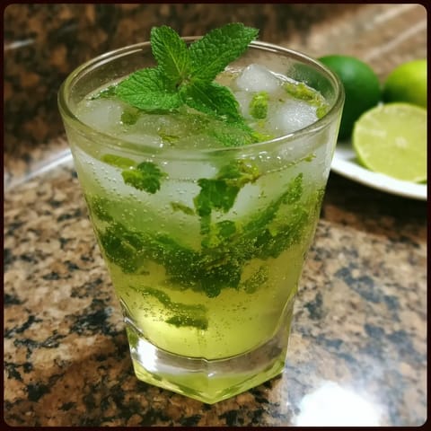 Widać wizerunek szklanki zawierającej napój złożony z jagód i liści mintu. Wizerunek jest wyraźny i jasny, a szklanka jest pełna.