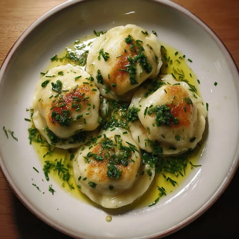 Na tle ciemnego tła, na białym talercie, siedzą trzy Tatra Cheese Dumplings z Chive Oil.
