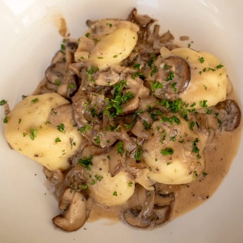 Golden-brown potato dumplings, plated and smothered in a creamy, savory mushroom sauce.