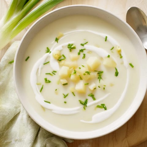 Garnished with fresh chives, this creamy Potato Leek Soup features a smooth, velvety texture in a rustic white bowl.