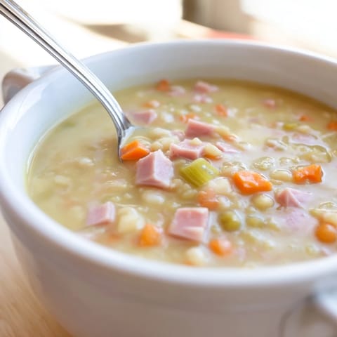 Gotowana zupa grochowa z szynką w garnku, z dodatkiem marchewki i selera.