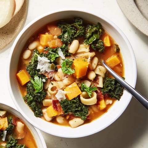 A close-up of hearty Fall Minestrone, showcasing tender kale, diced pancetta, and creamy white beans in a savory tomato-based broth.
