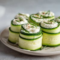 Na tle szarości widać siedem cucumber roll-ups z cream cheese.