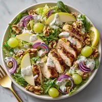 A plate of food with chicken, apples, and grapes.