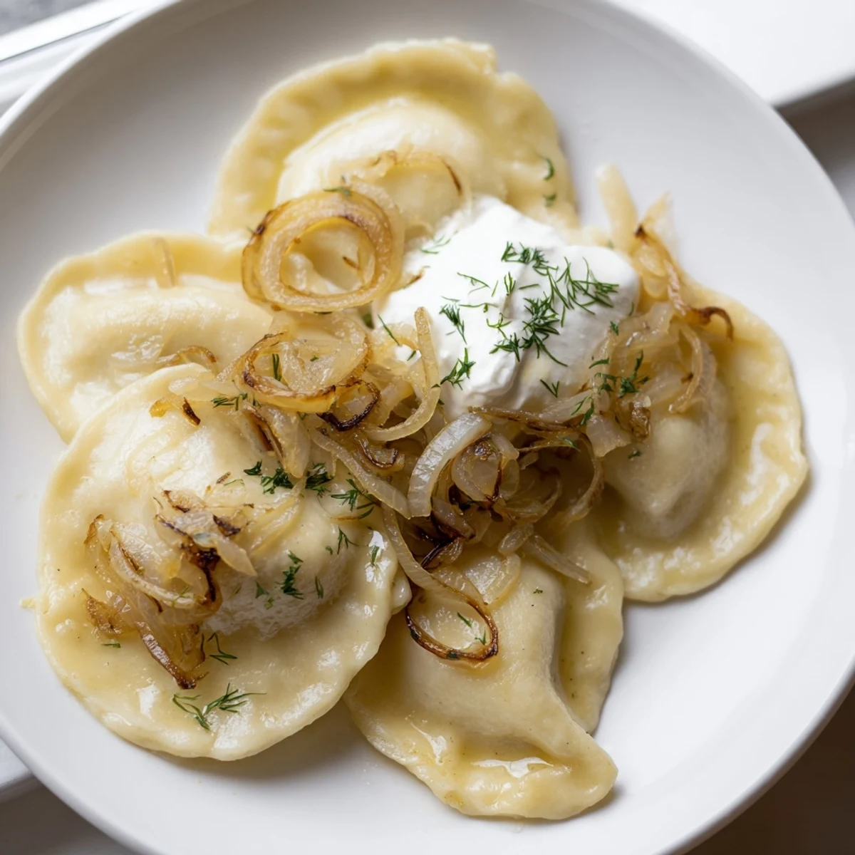 Golden fried Authentic Potato and Cheese Pierogi Ruskie, served hot with sour cream and fried onions.