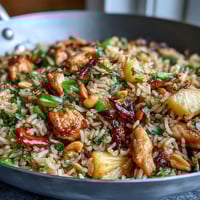 Talerz pełny tropikalnego ryżu smażonego z kawałkami kurczaka, ananasa i kolorowych warzyw, ozdobiony orzeszkami nerkowca.  